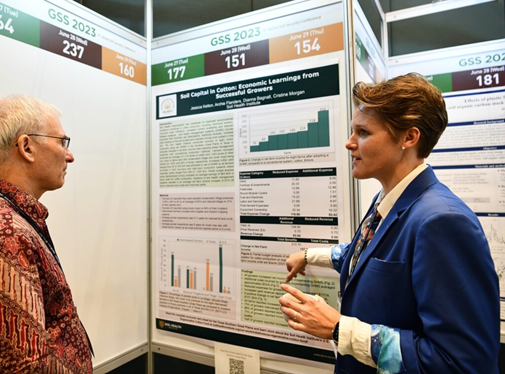 Dianna Bagnall points to a poster displayed at a conference while explaining it to an onlooker.