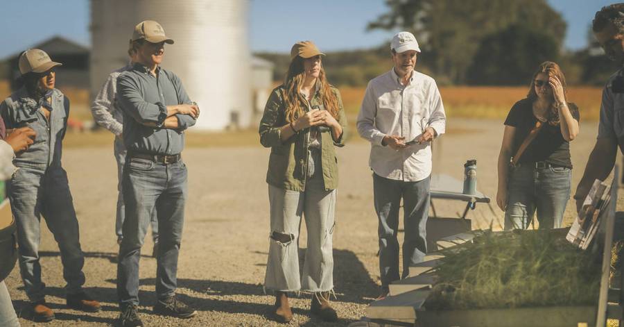 A group watches a speaker outdoors at a farm.